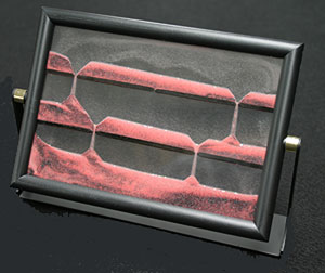 Coloured sand is encapsulated in liquid between sheets of glass. When the frame is inverted the sand